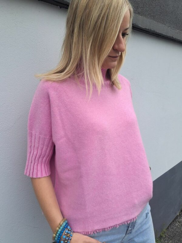 pull à col roulé rose à manches courtes et à la coupe cintrée, avec petite frange sur les bords.